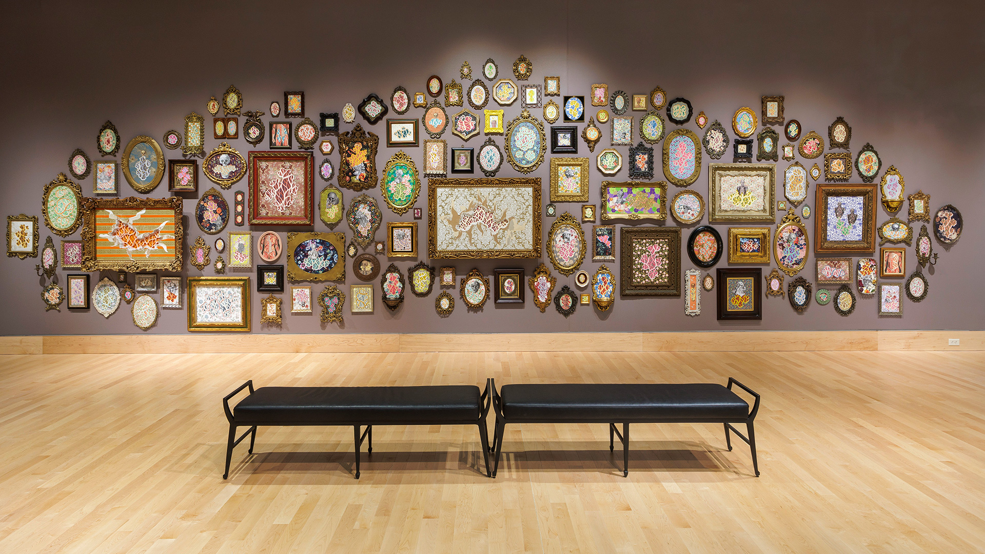 Framed paper cut outs on a gallery wall with two benches in front