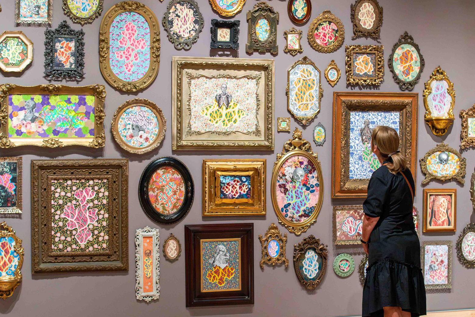 A woman looks at a wall full of fancy picture frames holding vibrant artwork