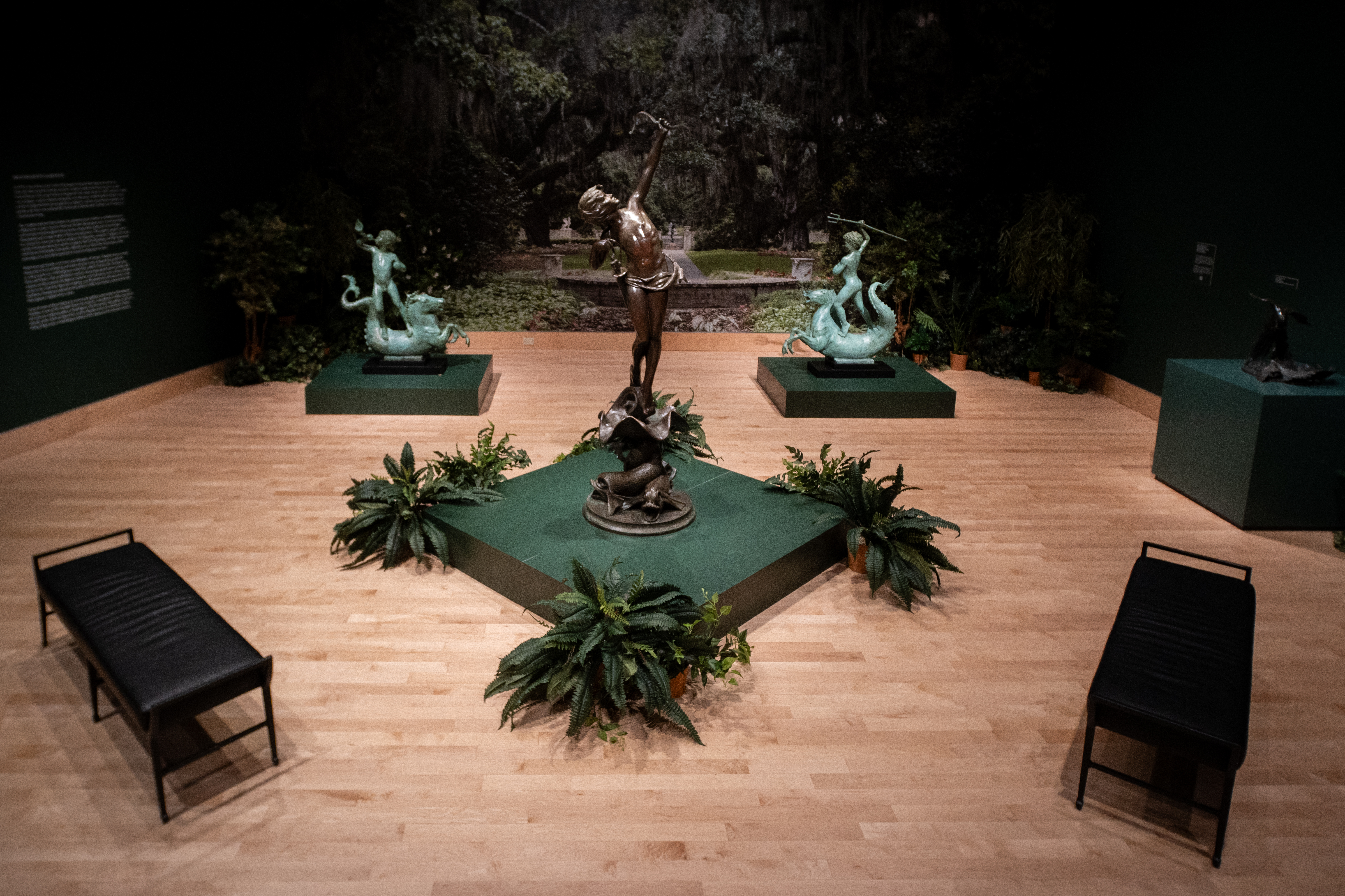 A sculpture of Diana aims a bow at the sky surrounded by foliage and two other sculptures in the background