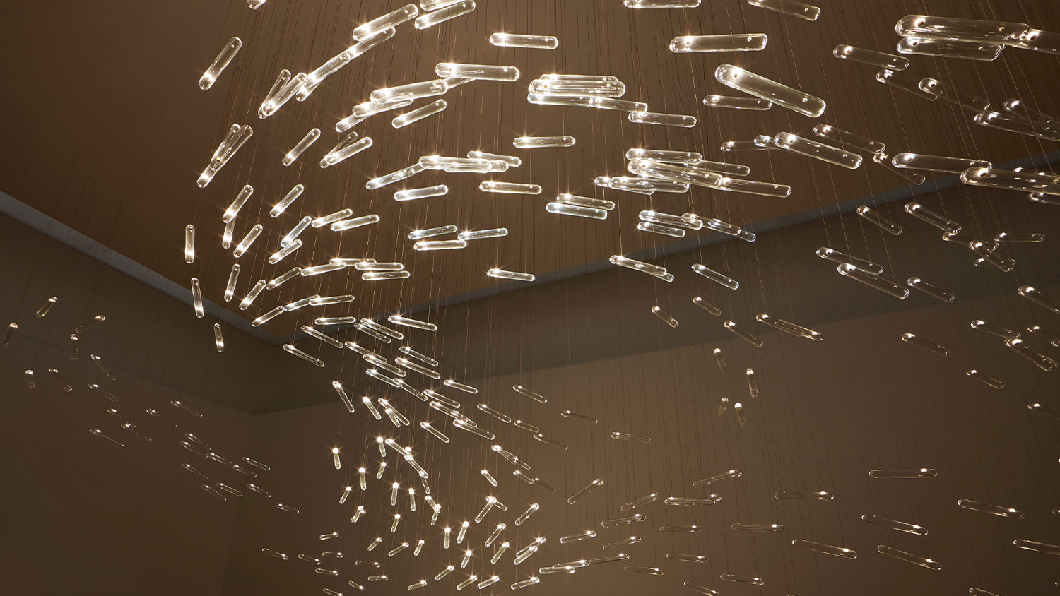 Art installation featuring glass cylinders hung from the ceiling with tiny lights inside