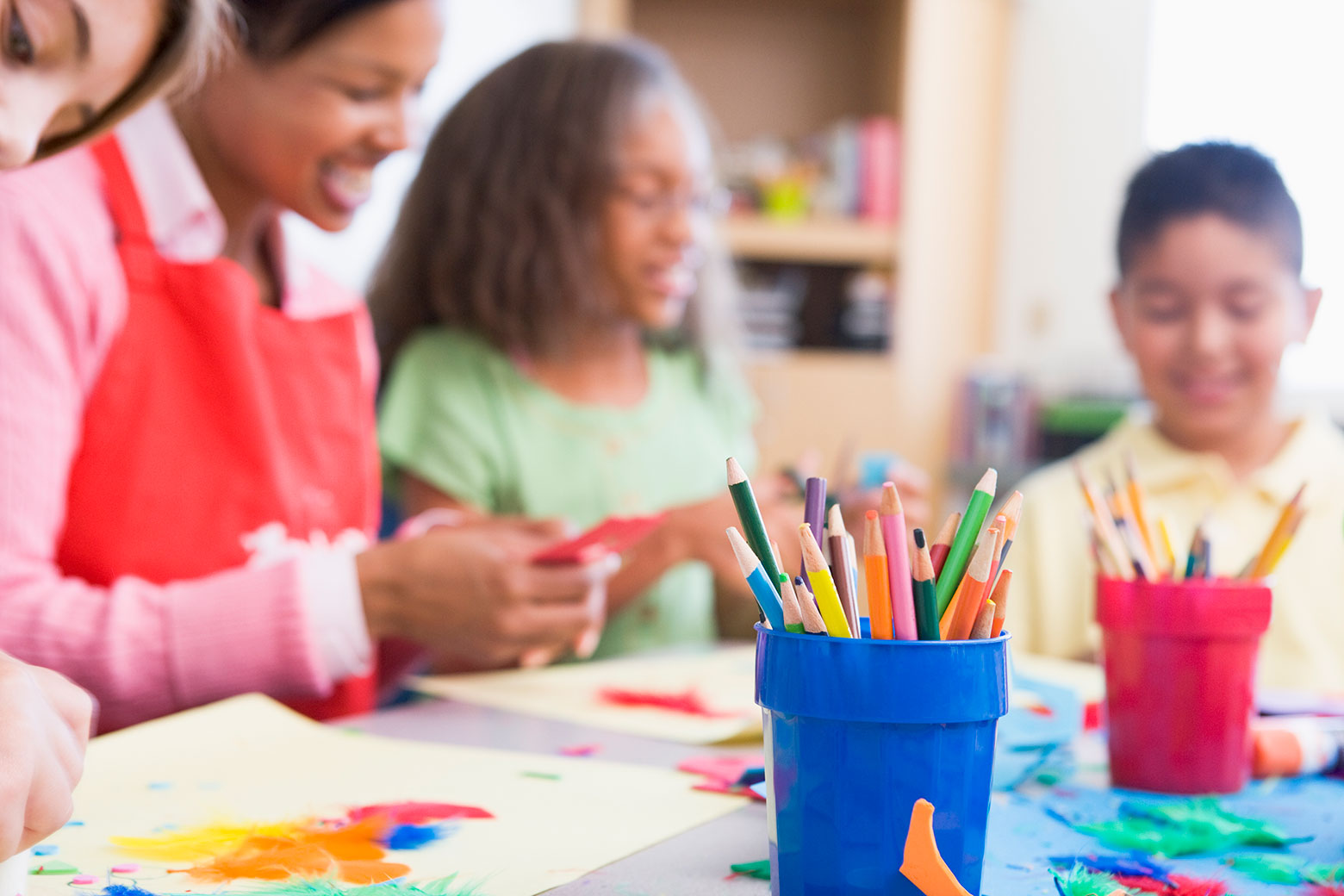 A teacher instructs students with colored pencils in the foreground