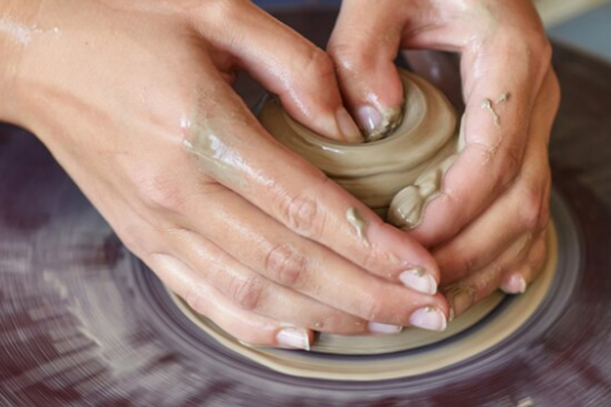 Closeup of hands forming clay on a pottery wheel